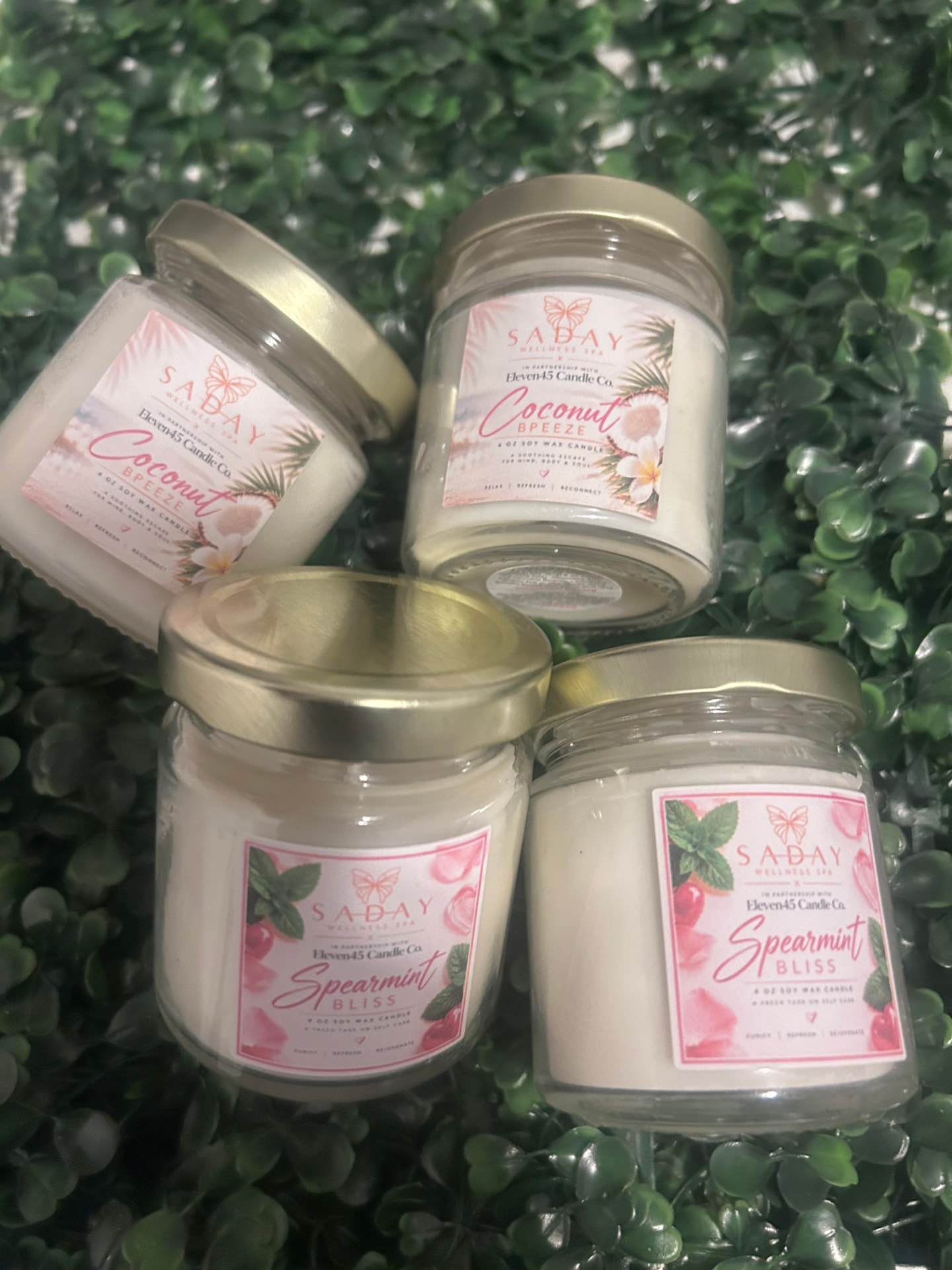Four gold-lid jar candles labeled Coconut Breeze and Spearmint Bliss, made for Saday Wellness Spa in partnership with Eleven45 Candle Co.