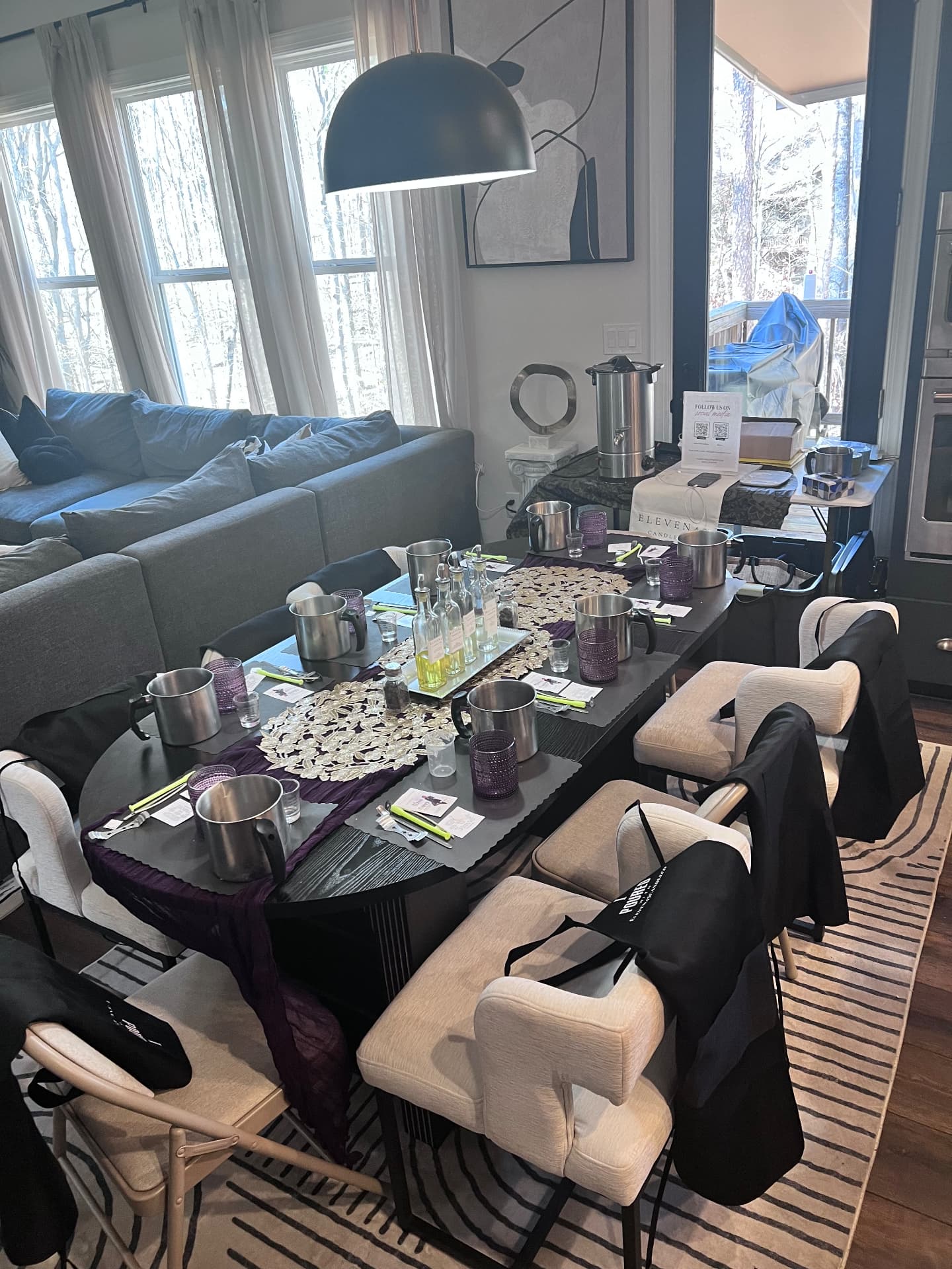 A dining table styled with purple runners, gold lace placemats, pouring pitchers, and fragrance bottles, with aprons draped over each chair
