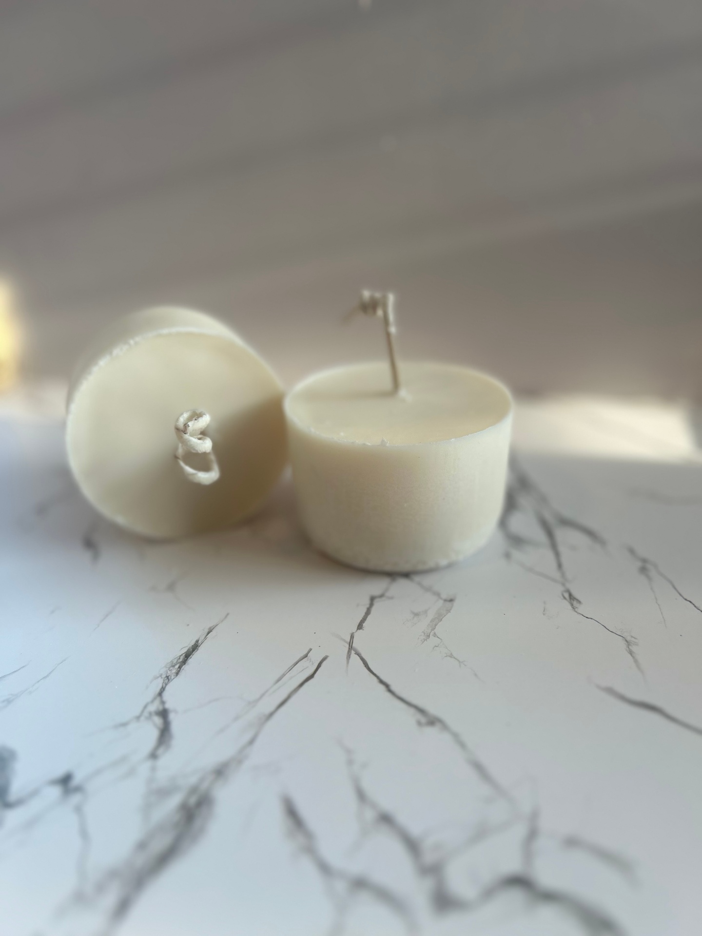 Two cream-colored soy wax candle refills on a white marble surface